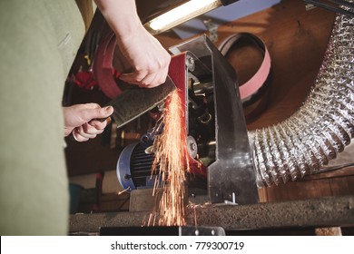 Making of a knife. Master sharpens a blade on the machine closeup in the Studio