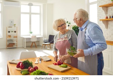 Making meals with love. Happy senior couple cooking healthy salad together in the kitchen of their modern studio apartment. Smiling mature husband helping his wife who's chopping vegetables for lunch - Powered by Shutterstock