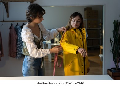 Making Measures Before Tailoring. Fashion Designer Workshop With Female Tailor Measuring And Fitting Bespoke Rain Jacket. Young Woman Small Dressmaking Business Owner At Workplace. Needlework Concept 