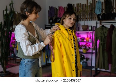 Making Measures Before Tailoring. Fashion Designer Workshop With Female Tailor Measuring And Fitting Bespoke Rain Jacket. Young Woman Small Dressmaking Business Owner At Workplace. Needlework Concept 