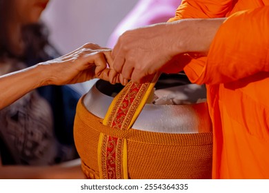 Making merit concept, Selective focus of alms bowl with yellow robe of cleric, Offer or give food to a Buddhist monk, Asian women's hand puting food offerings into a monk's bowl in early morning day.