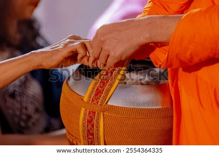Making merit concept, Selective focus of alms bowl with yellow robe of cleric, Offer or give food to a Buddhist monk, Asian women's hand puting food offerings into a monk's bowl in early morning day.
