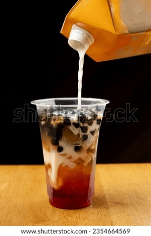 Making milk bubble tea with tapioca pearls in cafe over black background. Copy space