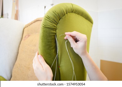 Making new upholstery on old armchair. Green velvet fabric. Restoration of old chair. Woman hands, working in upholstery workshop. Repairing old furniture. Hand sewing fabric.