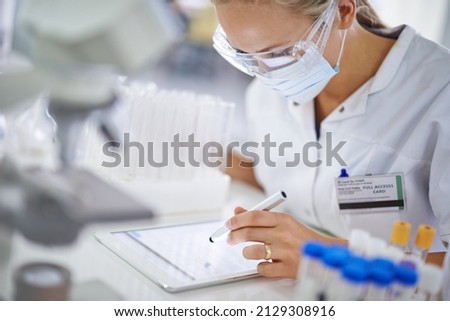 Making notes for her thesis. A young researcher recording her findings on a tablet in the lab.