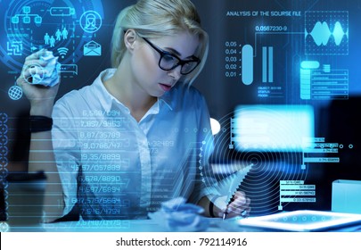 Making notes. Smart qualified experienced worker sitting in front of a big modern transparent screen and looking concentrated while making important notes in her notebook