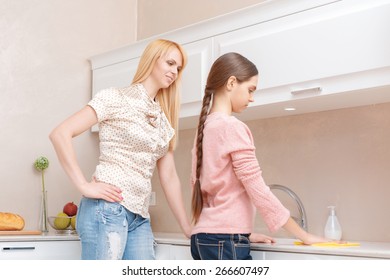 Making Order. Young Mother Supervises How Her Teen Daughter Is Cleaning The Kitchen Counter With A Cloth