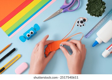 Making an origami shrimp out of orange paper. Women's hands attach an eye to a paper toy. Hobby idea. - Powered by Shutterstock