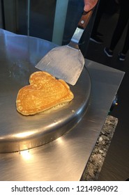 Making A Pancake On An Iron Pan. Heart Shaped. Homemade. Hand On The Flipper.