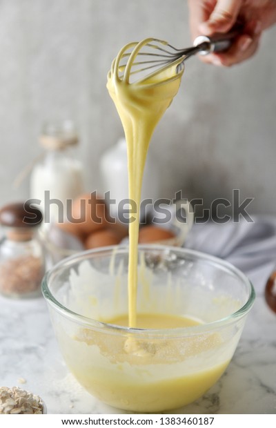 Making pancakes, cake, baking side view of\
baker hands pouring batter and whisking batter in bowl. Concept of\
Cooking ingredients and method on white marble background, Dessert\
recipes and homemade.