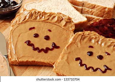 Making peanut butter sandwiches with personality! Fun smiley faces drawn on with jam. Creamy peanut butter with jam on whole grain wheat bread on wood cutting board. Macro with shallow dof. - Powered by Shutterstock