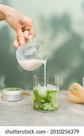 Making the perfect iced matcha latte. Pouring milk in glass with matcha - Shutterstock ID 2010256379