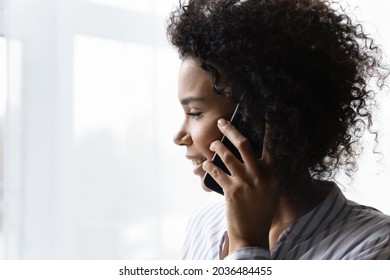 Making Phone Call. Close Up Profile Shot Of Smiling Young Afro American Woman Holding Mobile Phone Close To Ear. Mixed Race Female Standing By Window Engaged In Telephone Talk Conversation. Copy Space