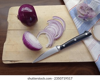 Making pickled red onions. Red onion, red onion slices and a knife on a wooden cutting board. Mason jar half-full with red onion slices and a lid is aside on a striped kitchen towell. - Powered by Shutterstock