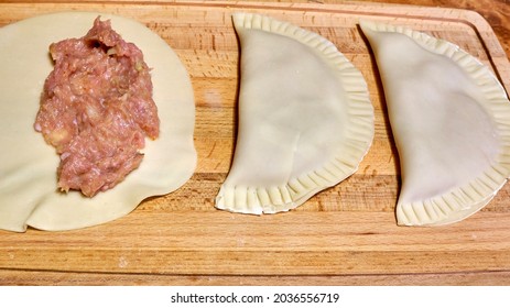 Making pies with meat in her home kitchen. Raw dough and meat for baking in the oven, process of making pies or dumplings. raw pies with meat on a white table in the kitchen, homemade pies
