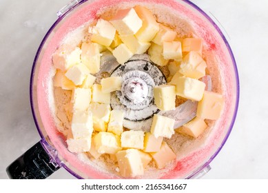 Making Pink Strawberry PIe Crust In A Food Processor: Overhead View Of Cubed Butter, Powdered Strawberries, And Flour In A Food Processor Bowl