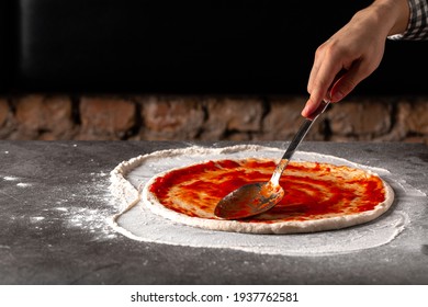 Making A Pizza Spreding Tomato Sauce On The Dough On The Grey Concrete Background