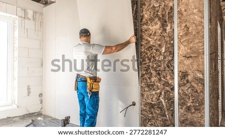 Making a plasterboard partition. A worker is laying drywall board on a metal support structure of partition.