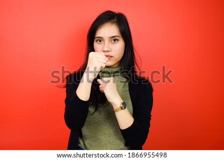 Making punch fist gesture of Young beautiful asian women using black sweater with red isolated background