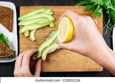 Making Raw Food Snack. Female Hands Squeeze Lemon Juice Onto Avocado Sandwich, Top View Shot