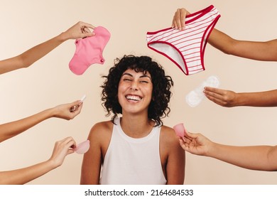 Making the right feminine hygiene choice. Happy young woman smiling at the camera while surrounded by hands holding different disposable and non-disposable sanitary products. - Shutterstock ID 2164684533