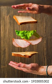 Making A Sandwich. Cheese, Bread And Meat Hang In The Air In Parts On A Wooden Background