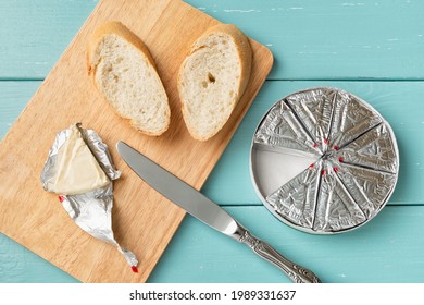 Making sandwich with processed cream cheese and sliced bread on a cutting board over blue wooden table. Small triangular pieces of soft cheese wrapped with aluminium foil. Tasty breakfast. Top view. - Powered by Shutterstock