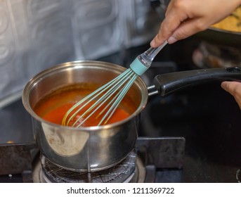 Making sauce in a saucepan using an egg beater utensil.