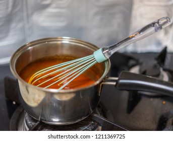 Making sauce in a saucepan using an egg beater utensil.