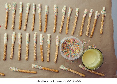 Making Simple Snacks For A Birtday Party - Sesame Sticks Dipped In White Chocolate With Colorful Sprinkles. Top Down View.