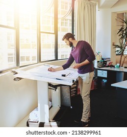 Making some adjustments. Full length shot of a young architect working on his drafting table.