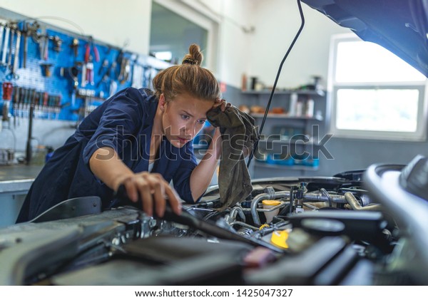 Making some adjustments to her car. Portrait Of\
Female Auto Mechanic Working. Mechanic repairs the engine of a car\
in her workshop. Mechanic examining under hood of car at the repair\
garage