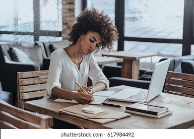 Making some notes. Thoughtful young African woman writing something down while sitting in restaurant - Shutterstock ID 617984492