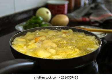 Making A Spanish Omelette, Potato And Onion. You Can See A Small View Of The Kitchen With Various Utensils, Potatoes, Onions, Peppers, A Wooden Spoon And A Dishcloth.