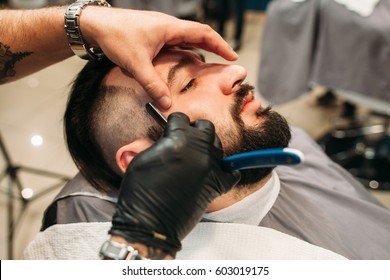 Making Stylish Curly Haircut At Salon Closeup. Man Sitting With Closed Eyes While Barber Shaving Him With Razor. Beauty, Modern Style, Lifestyle, Trend Concept