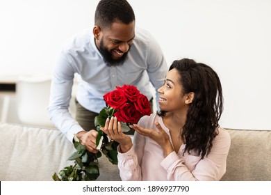 Making Surprise. Excited black girlfriend receiving bouquet of red roses from her happy boyfriend who holding bunch of flowers and greeting her with St Valentine's or International Women's Day