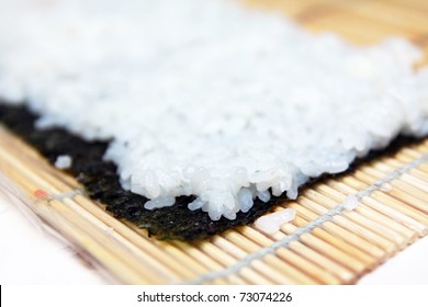Making sushi roll on wooden mat, closeup