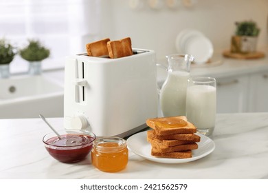 Making toasts for breakfast. Appliance, crunchy bread, honey, jam and milk on white marble table in kitchen - Powered by Shutterstock