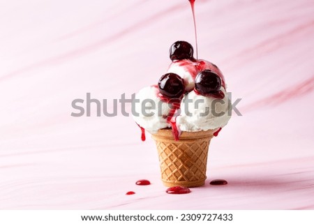 Making vanilla ice cream scoop in a serve waffle cone with canned cherries and flowing cherry syrup on a pink background, copy space.