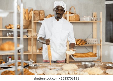 Making yeast dough in bakery - male baker rolling out dough with a rolling pin - Powered by Shutterstock