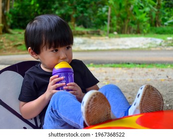 MALACCA,MALAYSIA - MAC 12, 2021: A Cute Asian Kid Wearing Black Shirt Drinking Fresh Water From Purple Colored BPA Free Bottle