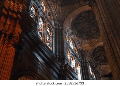 Malaga Catedral Interior of a cathedral or large church, architectural features include high vaulted ceilings, intricate stonework, and tall stained glass windows, colorful light to filter through - Powered by Shutterstock