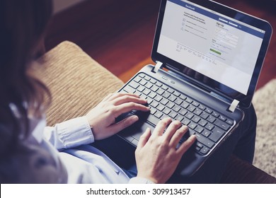 MALAGA, SPAIN - APRIL 26, 2015: Facebook Login Page In A Computer Screen. Woman Holding A Laptop On Her Knees While Type On The Keyboard. Facebook Is The Most Famous Social Website All Over The World.