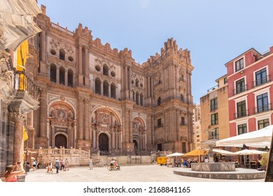 Malaga, Spain, June 10, 2022; View Of The Facade Of The Malaga Cathedral Or Santa Iglesia Catedral Basílica De La Encarnación, With A Fountain And Tourists In The Town Square In The Foreground.