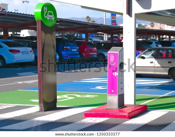 Malaga/Spain -\
03-25-2019 : on an outdoor car parking, one empty spot with ground\
painted in green with an illustration in white indicating a\
charging station for electric\
cars.