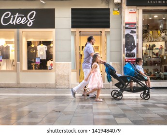 Malaga/Spain - 06-08-2019 : Man Pushing A Double Stroller And Two Kids In It, A Young Girl Is Walking Next To Him On A Pedestrian Street.