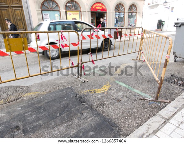 Malaga/Spain - 12-25-2018 :\
traffic safety metallic yellow barriers with some red and white\
tape . They are disposed on the road, downtown, around a car\
parking spot.