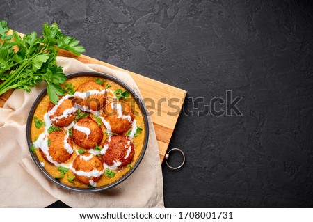 Malai Kofta Curry in black bowl at dark slate background. Malai Kofta is indian cuisine dish with potato and paneer cheese deep fried balls in onion tomato gravy with spices. Indian Food. Copy space