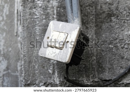 Malang, East Java, Indonesia - 2026. Old Double Light Switch On Concrete Wall. White plastic switch panel covered with cement splashes. Exposed wires and conduit pipe on rough concrete surface. Perfect for construction, electrical work, and building repair concepts.