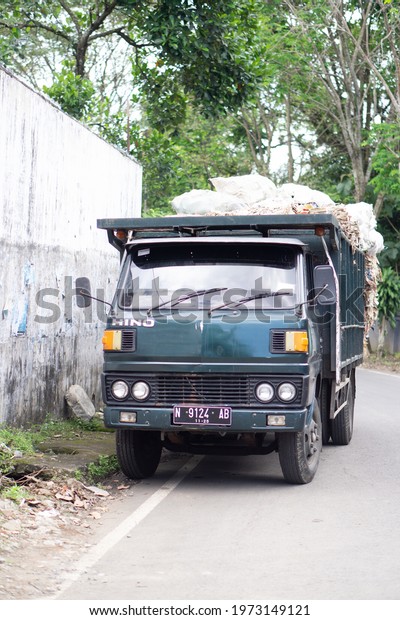 Malang, Indonesia - March\
25, 2021: A dark green truck with a full load is parked on the side\
of the road.